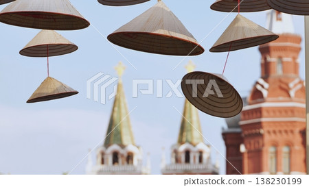 Traditional Asian conical hats hanging outdoors with a red brick historic tower in the background. 138230199