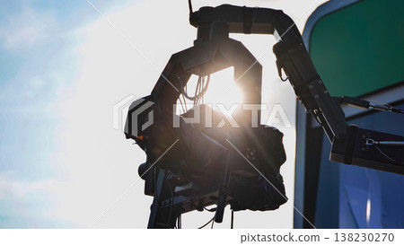 Professional video camera on a crane, silhouetted against a bright sun with lens flare. Professional video camera on a crane, silhouetted against a bright sun with lens flare. 138230270