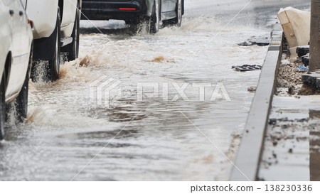 Rear car tire splashing muddy water from deep puddle on flooded urban street Rear car tire splashing muddy water from deep puddle on flooded urban street 138230336