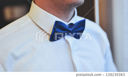 Groom preparing for wedding, smoothing blue bow tie with refined gestures, radiating sophisticated charm before ceremony begins Groom preparing for wedding, smoothing blue bow tie with refined gestures, radiating sophisticated charm before ceremony begins 138230363