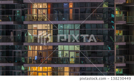 Rows of glowing windows with people in apartment building at night. Rows of glowing windows with people in apartment building at night. 138230449