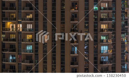 Rows of glowing windows with people in apartment building at night. Rows of glowing windows with people in apartment building at night. 138230450