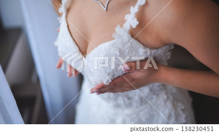 Intimate close up of a woman in a white wedding dress adjusting the bodice. Intimate close up of a woman in a white wedding dress adjusting the bodice. 138230451