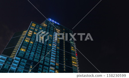 Night Sky with clouds above modern skyscraper with glowing windows architecture timelapse. Night Sky with clouds above modern skyscraper with glowing windows architecture timelapse. 138230599