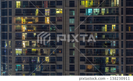 Rows of glowing windows with people in apartment building at night. Rows of glowing windows with people in apartment building at night. 138230911