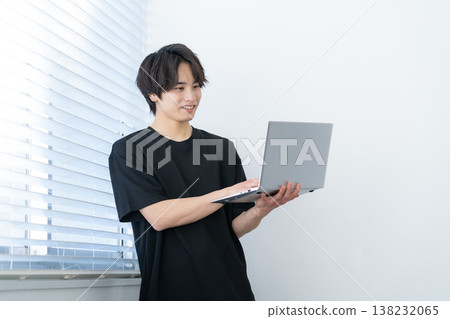 A young man looking at his computer by the window. A young man looking at his computer by the window. 138232065