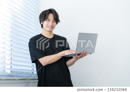 A young man looking at his computer by the window. A young man looking at his computer by the window. 138232066