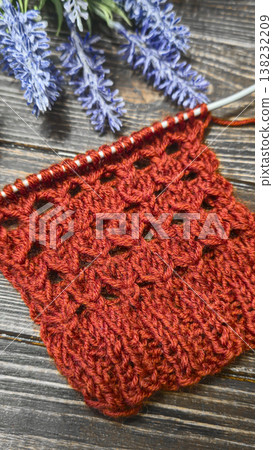 A relief openwork pattern knitted with colored yarn on a wooden background A relief openwork pattern knitted with colored yarn on a wooden background 138232209