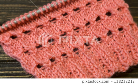 A relief openwork pattern knitted with colored yarn on a wooden background A relief openwork pattern knitted with colored yarn on a wooden background 138232212