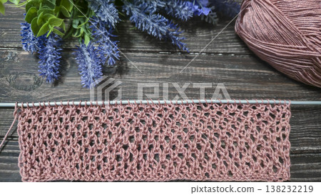 A relief openwork pattern knitted with colored yarn on a wooden background A relief openwork pattern knitted with colored yarn on a wooden background 138232219