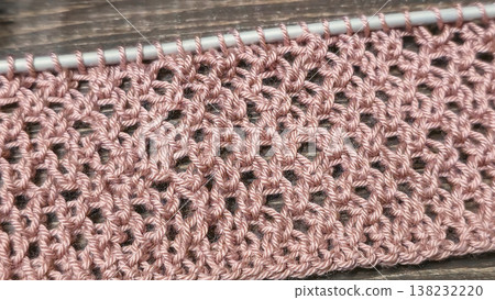 A relief openwork pattern knitted with colored yarn on a wooden background A relief openwork pattern knitted with colored yarn on a wooden background 138232220