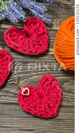 Red knitted heart-shaped keychain on a wooden background. Handmade. Red knitted heart-shaped keychain on a wooden background. Handmade. 138232238
