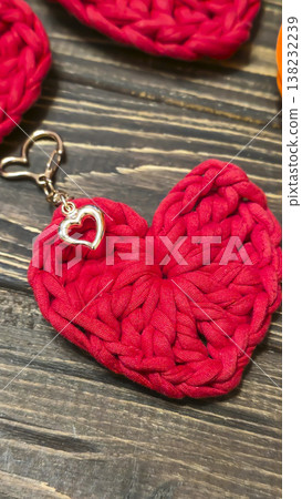 Red knitted heart-shaped keychain on a wooden background. Handmade. Red knitted heart-shaped keychain on a wooden background. Handmade. 138232239