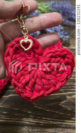 Red knitted heart-shaped keychain on a wooden background. Handmade. Red knitted heart-shaped keychain on a wooden background. Handmade. 138232241