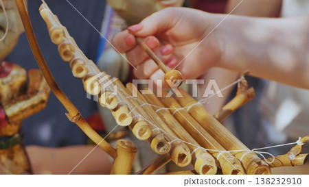 Close up of a hand playing a traditional handmade bamboo xylophone musical instrument 138232910