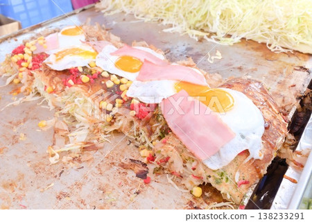 Okonomiyaki topped with a fried egg cooked on a griddle, a finished product of street food. 138233291