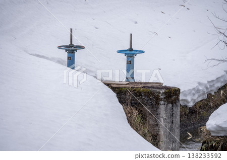 A blue sluice gate standing in a snow-covered waterway, a scene of melting snow. A blue sluice gate standing in a snow-covered waterway, a scene of melting snow. 138233592
