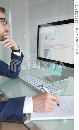Businessman in a blue jacket thinking and brainstorming ideas while working on computer and taking notes in modern office. Business people concept 138233741