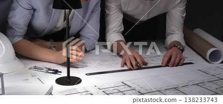 Architects collaborating on blueprints, diligently planning building design and construction project details late at night. 138233743