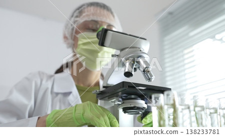 Scientist analyzing test tubes, wearing green protective gear while working with microscope in sterile laboratory research environment. Medicine, healthcare and science concept Scientist analyzing test tubes, wearing green protective gear while working with microscope in sterile laboratory research environment. Medicine, healthcare and science concept 138233781