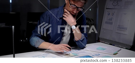 Man analyzing financial charts and business data on tablet in late night office, working overtime on a new project, thinking about solution and strategy Man analyzing financial charts and business data on tablet in late night office, working overtime on a new project, thinking about solution and strategy 138233885