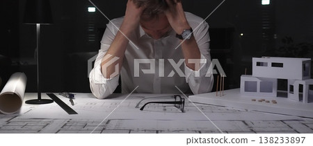 Architect experiencing burnout and stress, working late at night in a dark office with building models and blueprints. Architect experiencing burnout and stress, working late at night in a dark office with building models and blueprints. 138233897