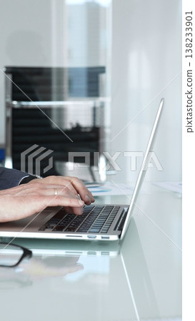 Businessman in a modern office intently typing on a laptop, deeply focused and analyzing data to develop solutions and strategies for projects and corporate challenges Businessman in a modern office intently typing on a laptop, deeply focused and analyzing data to develop solutions and strategies for projects and corporate challenges 138233901