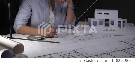 Architect analyzing blueprints and architectural scale model, planning a modern house construction project. Business and architect people concept Architect analyzing blueprints and architectural scale model, planning a modern house construction project. Business and architect people concept 138233902