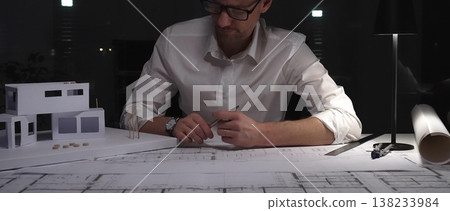 Architect working late on building plans and a residential house model, designing a new construction project. Business and architect people concept 138233984