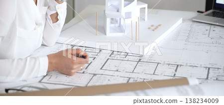 Female architect engrossed in architectural plans and miniature scale model, thoughtfully designing a new building project for modern construction development Female architect engrossed in architectural plans and miniature scale model, thoughtfully designing a new building project for modern construction development 138234009