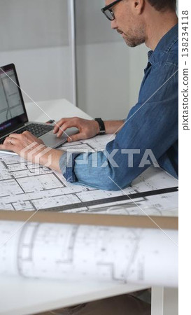 Architect hands reviewing building blueprints and housing plans on a table, utilizing a laptop for architectural drawing and design while planning a construction project Architect hands reviewing building blueprints and housing plans on a table, utilizing a laptop for architectural drawing and design while planning a construction project 138234118