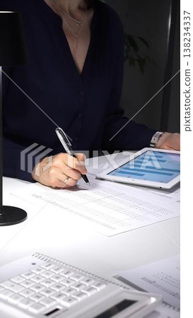 Woman using a tablet with charts and graphs, working late to analyze data and economic statistics for business growth. Audit and taxes theme in business 138234337