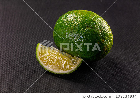 Fresh whole lime and a juicy cut wedge on a dark textured background Fresh whole lime and a juicy cut wedge on a dark textured background 138234934