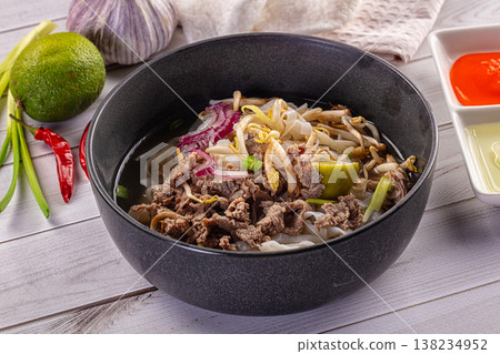 Vietnamese Pho Bo noodle soup with beef, bean sprouts and herbs in a dark bowl on a white wooden table Vietnamese Pho Bo noodle soup with beef, bean sprouts and herbs in a dark bowl on a white wooden table 138234952