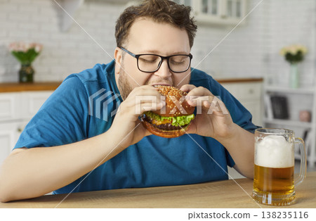 Plus-size man enjoying burger and beer at home kitchen, cheat meal concept Plus-size man enjoying burger and beer at home kitchen, cheat meal concept 138235116