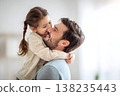 Little girl kissing her father's cheek while embracing him, both smiling and sharing a loving moment together, representing family bonding, joy, and affectionate parenting 138235443