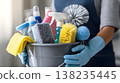 Person wearing protective gloves holding a bucket packed with essential cleaning products, illustrating the concept of domestic housework, professional cleaning service, and home maintenance 138235445