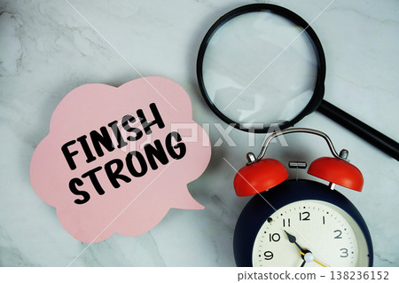 Finish Strong text with magnifying glass and alarm clock on marble background 138236152