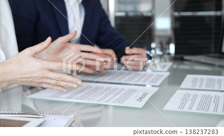 Close-up view of a business person in a professional office setting, reviewing and signing a legal contract document. Hands holding a pen over paperwork during corporate deal negotiations Close-up view of a business person in a professional office setting, reviewing and signing a legal contract document. Hands holding a pen over paperwork during corporate deal negotiations 138237283