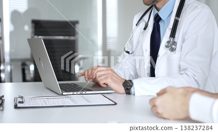 Doctor man in white coat and stethoscope consulting with a patient, writing notes on a clipboard during an appointment. Medicine, healthcare and science concept Doctor man in white coat and stethoscope consulting with a patient, writing notes on a clipboard during an appointment. Medicine, healthcare and science concept 138237284