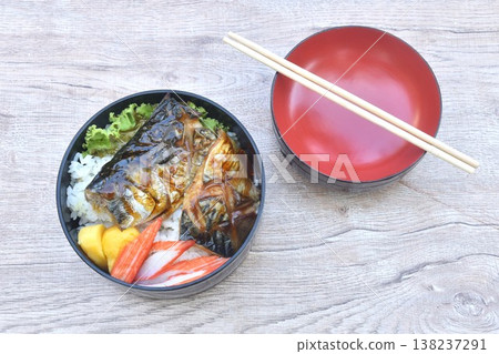 grilled saba fish or mackerel on rice topping sweet egg and crab stick couple lettuce salad bento set in lunch box on table 138237291