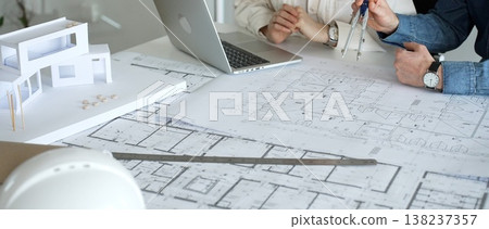 Architect working on a new building project, using a laptop to review digital blueprints and architectural models, creating modern house designs for urban development planning Architect working on a new building project, using a laptop to review digital blueprints and architectural models, creating modern house designs for urban development planning 138237357
