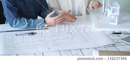 Architects discussing building plans, reviewing blueprints and architectural models, brainstorming design ideas for a new residential or commercial construction project Architects discussing building plans, reviewing blueprints and architectural models, brainstorming design ideas for a new residential or commercial construction project 138237366