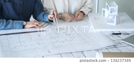 Architects discussing building plans, reviewing blueprints and architectural models, brainstorming design ideas for a new residential or commercial construction project Architects discussing building plans, reviewing blueprints and architectural models, brainstorming design ideas for a new residential or commercial construction project 138237389