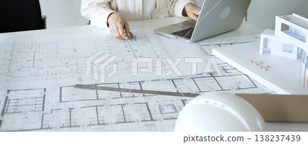 Architect working on a new building project, using a laptop to review digital blueprints and architectural models, creating modern house designs for urban development planning Architect working on a new building project, using a laptop to review digital blueprints and architectural models, creating modern house designs for urban development planning 138237439