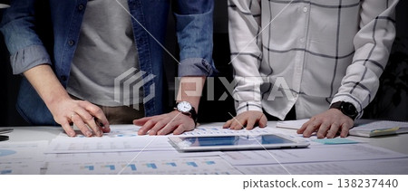 Business professionals analyzing financial data with charts and graphs on a tablet and paper, collaborating on market strategy and corporate growth planning in an office setting 138237440
