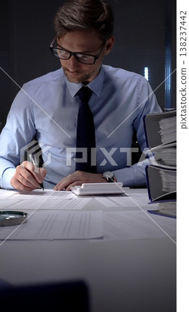 Businessman working meticulously with financial documents, using a pen and calculator to manage accounting tasks and reporting. Audit and taxes in business 138237442