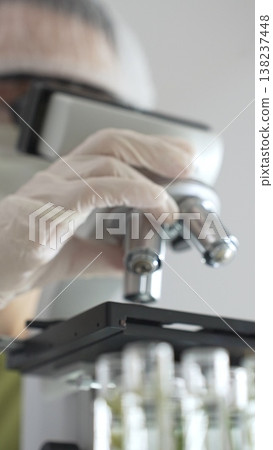 Close up of white gloved hand of a scientist adjusting a microscope in a laboratory. Medicine, health care and science concept 138237448