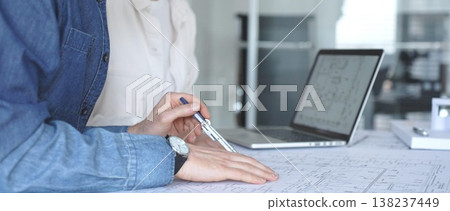 Architects collaborating on blueprint plans, discussing engineering details and project designs, planning construction development with a laptop in a modern office environment Architects collaborating on blueprint plans, discussing engineering details and project designs, planning construction development with a laptop in a modern office environment 138237449