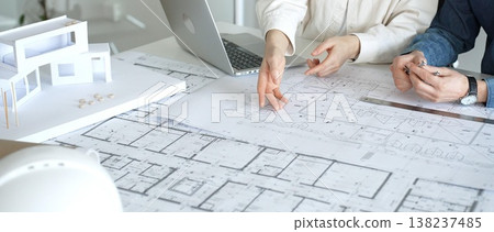 Architects and engineers collaborating on a housing project, designing building blueprints, planning new construction details, and discussing architectural models with a laptop on a desk Architects and engineers collaborating on a housing project, designing building blueprints, planning new construction details, and discussing architectural models with a laptop on a desk 138237485